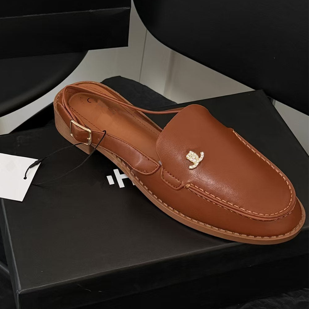 A brown leather slingback loafer with a small gold butterfly emblem on the toe, resting on a black shoebox.