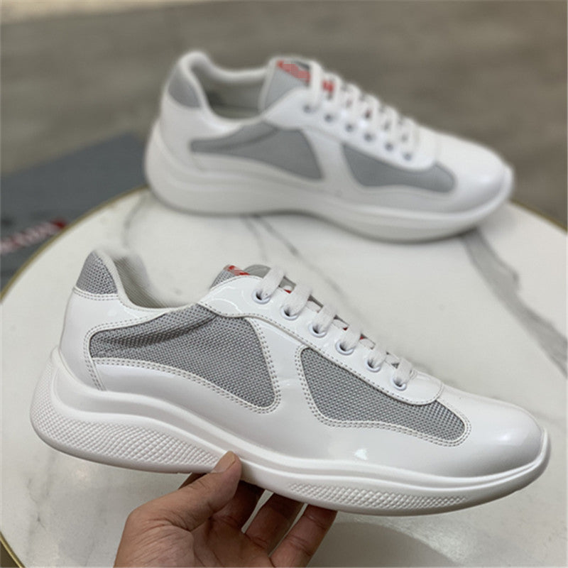 White sneakers with gray mesh panels held by a hand on a marble surface.