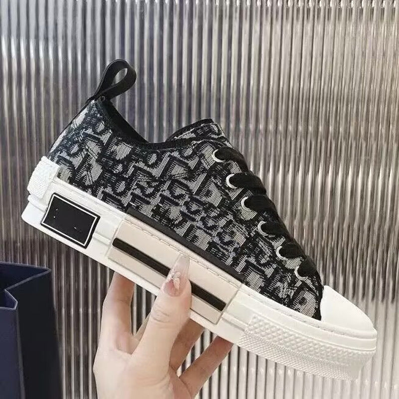 A hand holds a black and white monogram low-top sneaker against a metallic ribbed background.