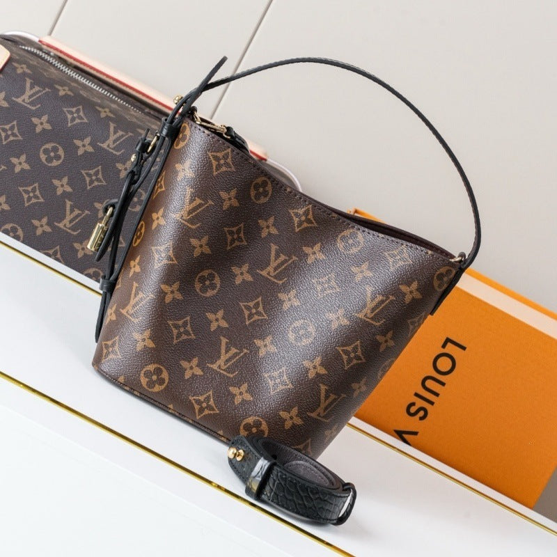Louis Vuitton monogram canvas handbag with a black leather handle and strap, displayed on a white surface with an orange Louis Vuitton box in the background.