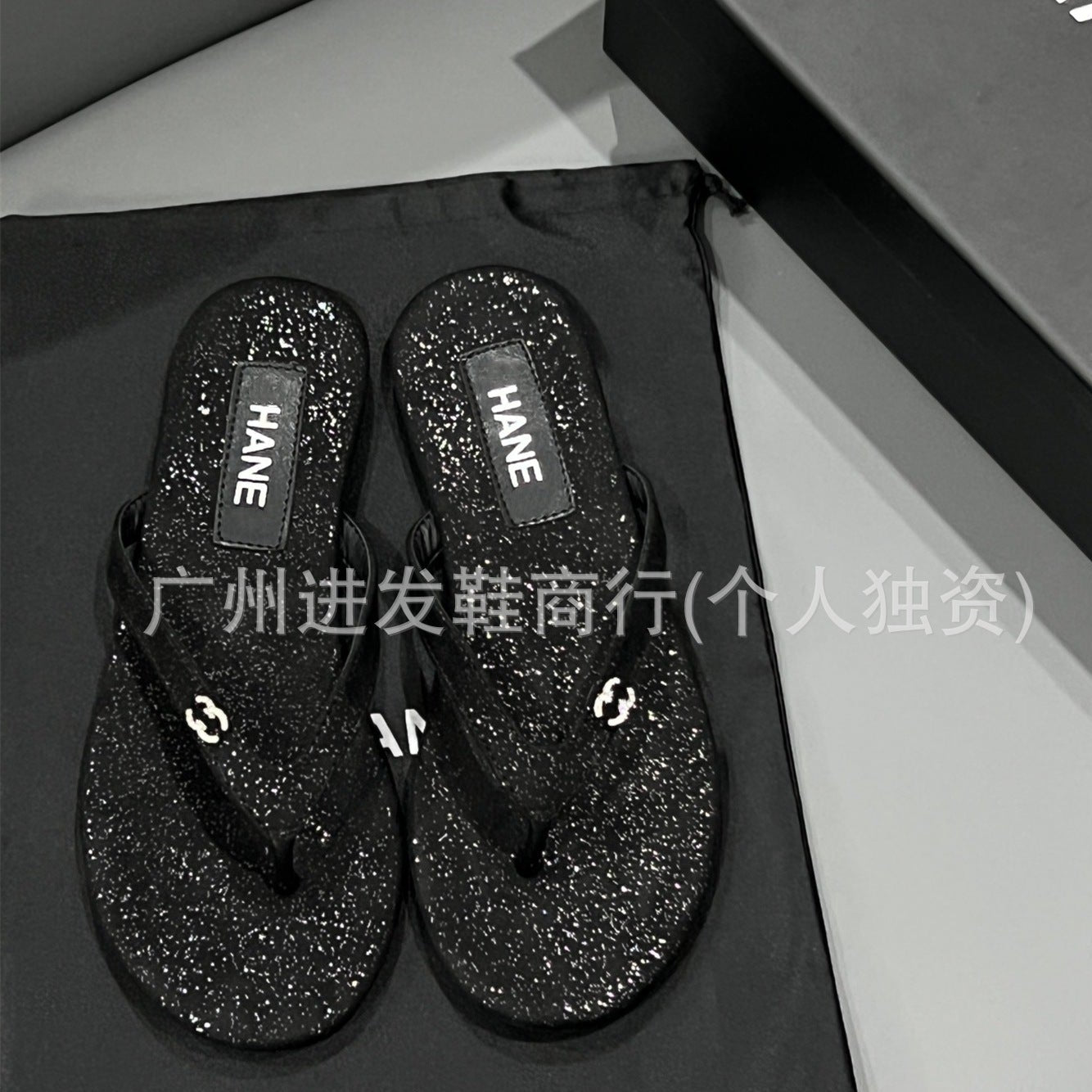 Black glittery flip-flops with 'HANE' branding on a black surface.
