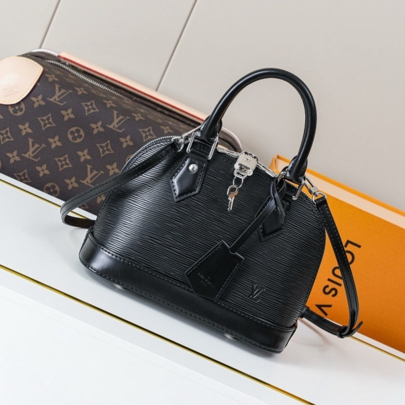 A black Louis Vuitton handbag with a textured monogram pattern, displayed on a white surface next to its signature orange box and a brown monogram pouch.