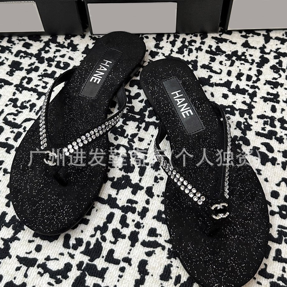 A pair of black glittery thong sandals with rhinestone-embellished straps and a small interlocking CC logo charm, displayed on a black-and-white spotted rug.