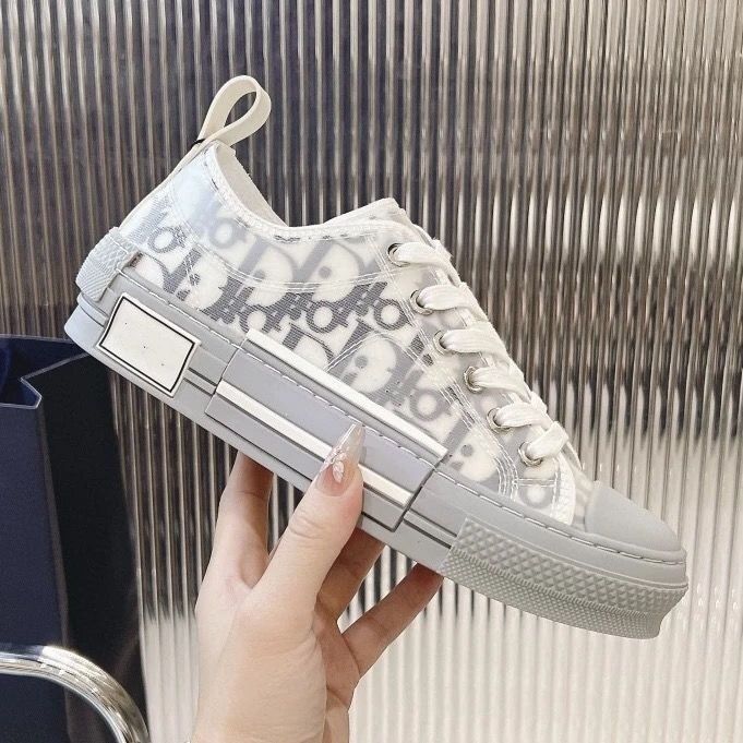 White sneaker with brand logo held by a hand against a metallic background