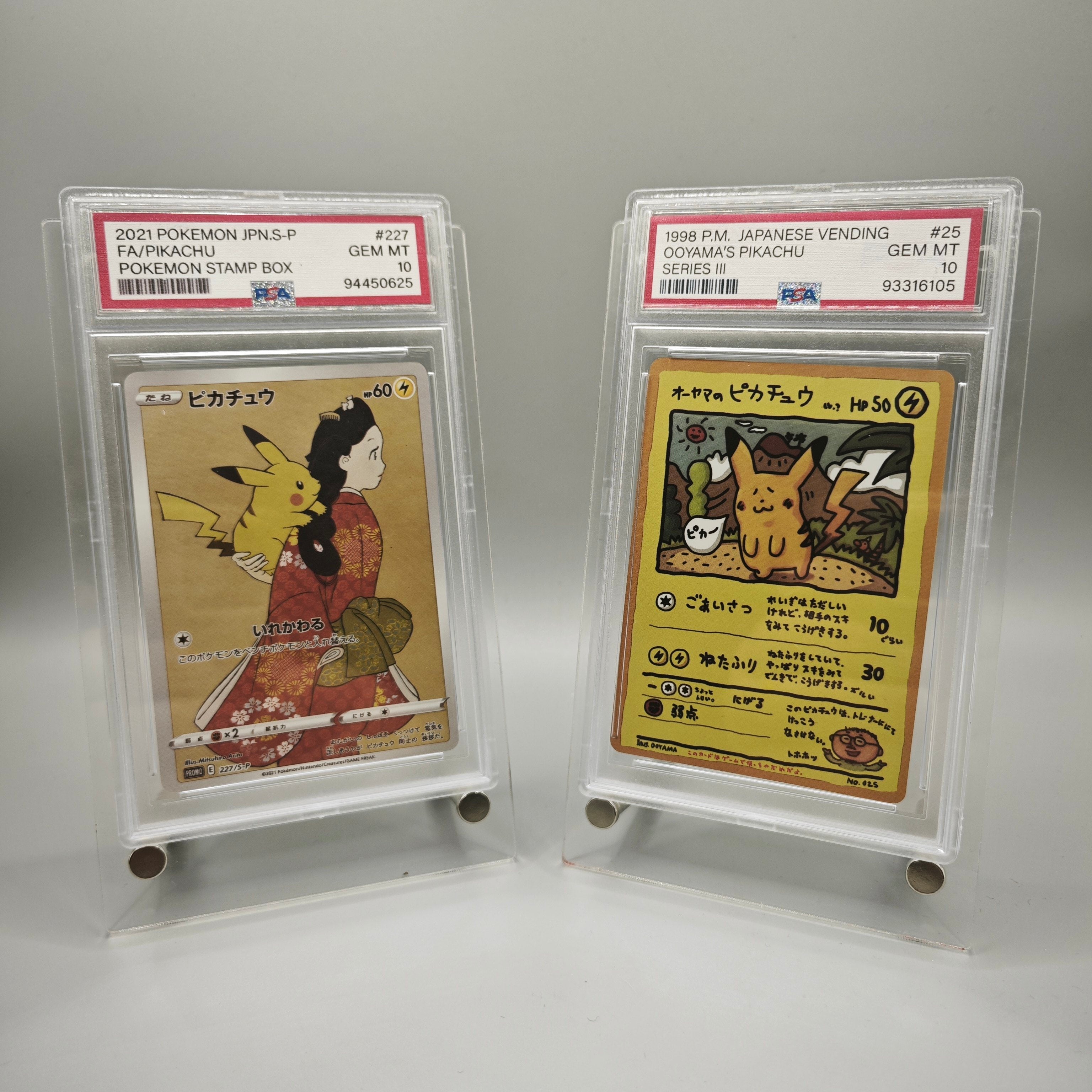 Two graded Pokémon trading cards in clear PSA-style holders on a light gray background. The left card is a 2021 Paldean Fates Paldean Stamp Box (JNIS.