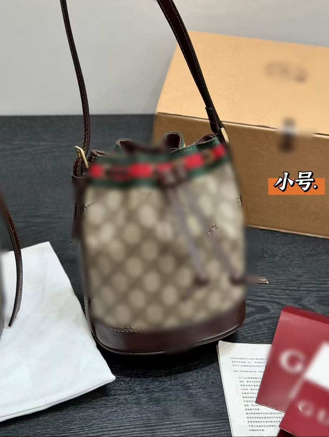 Designer handbag with visible brand logo on a dark surface with a box and paper in the background.