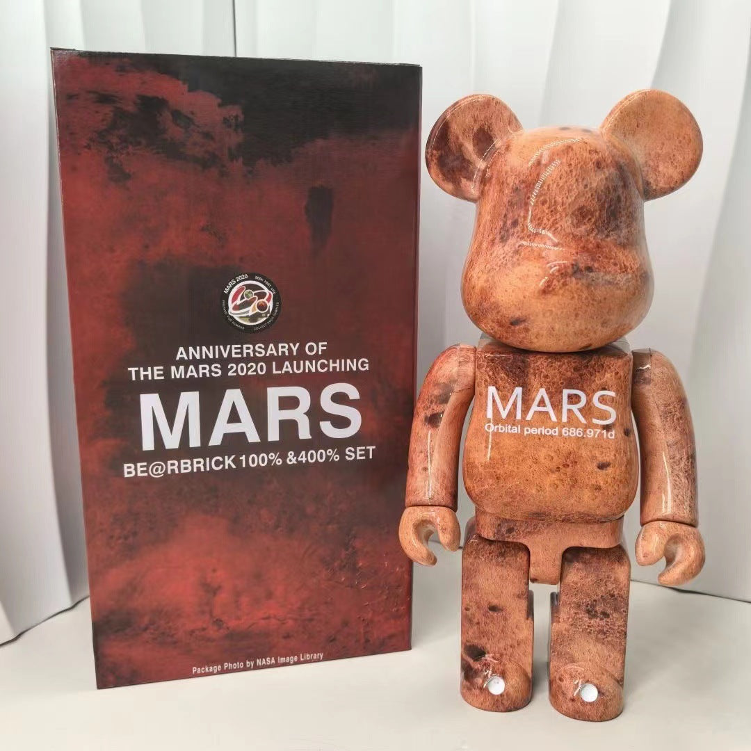 A BE@RBRICK 100% marble collectible bear figure with a distressed reddish-brown marble pattern and white 'MARS' text on its chest, standing next to its dark red and black packaging box.