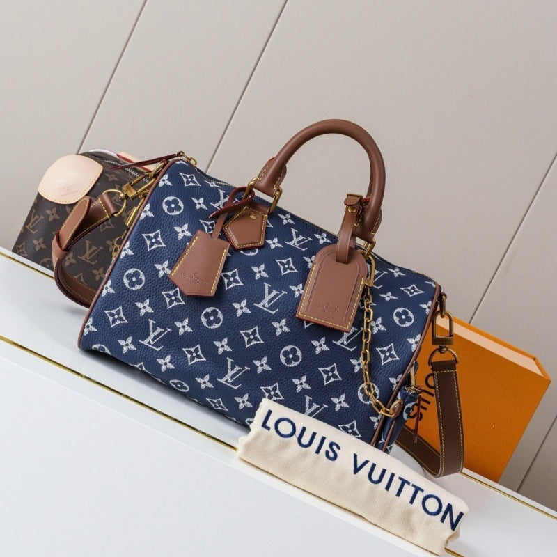 Louis Vuitton monogram canvas Speedy handbag in navy blue with brown leather handles and trim, displayed on a white shelf with a dust bag and orange box in the background.