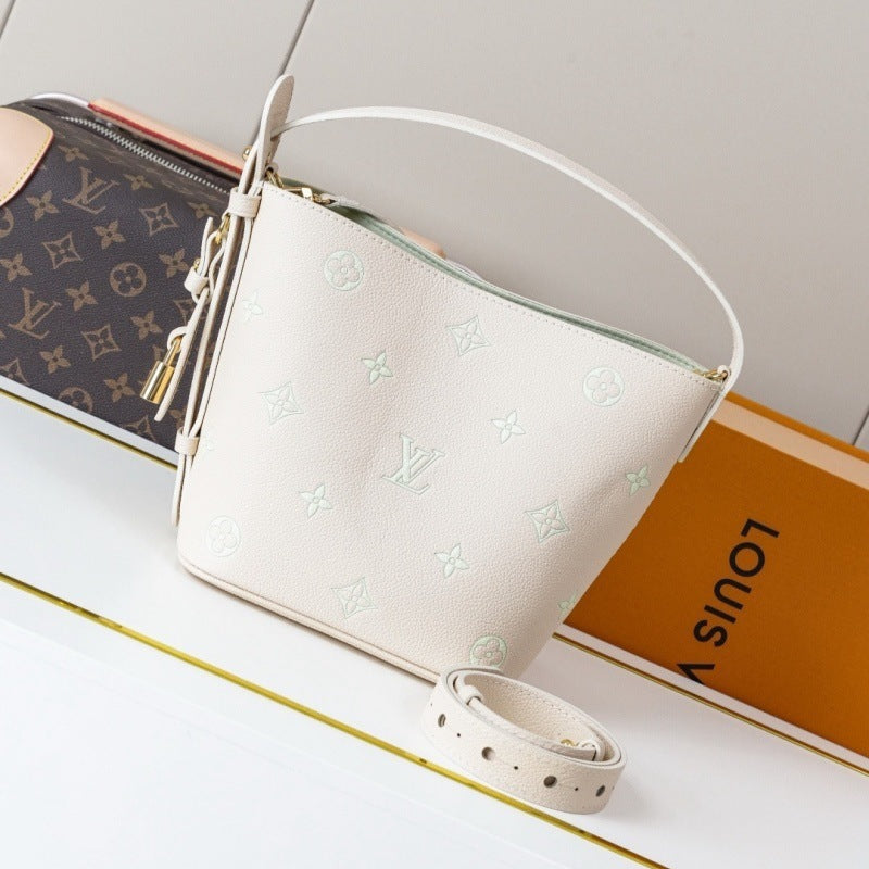 A Louis Vuitton shoulder bag in off-white monogram canvas with a top handle and detachable strap, displayed next to its brown monogram pouch and orange box on a white surface.