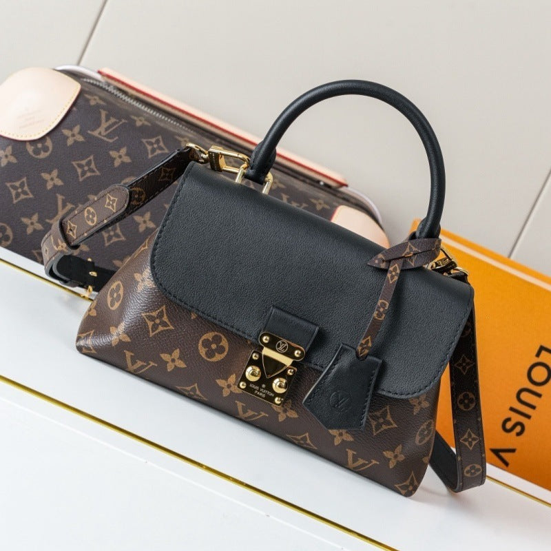 A Louis Vuitton handbag in the classic brown monogram canvas with black leather trim and a black top handle, displayed alongside a matching monogram duffel bag and an orange Louis Vuitton box on a white surface.