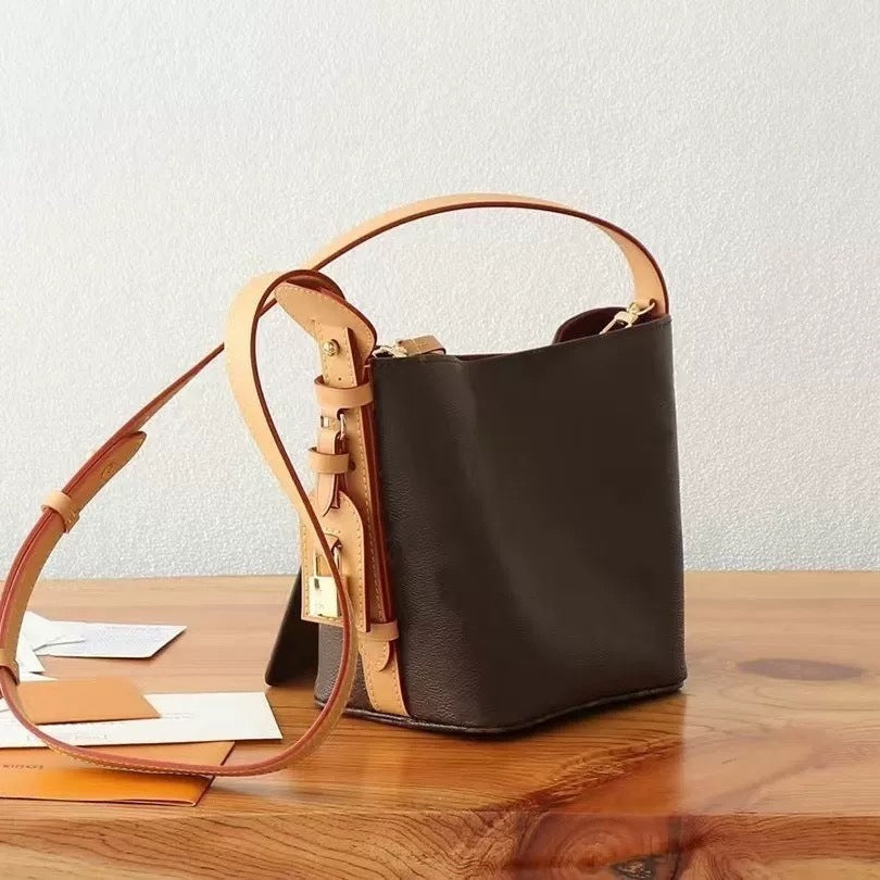 Brown leather handbag with tan handle on a wooden surface