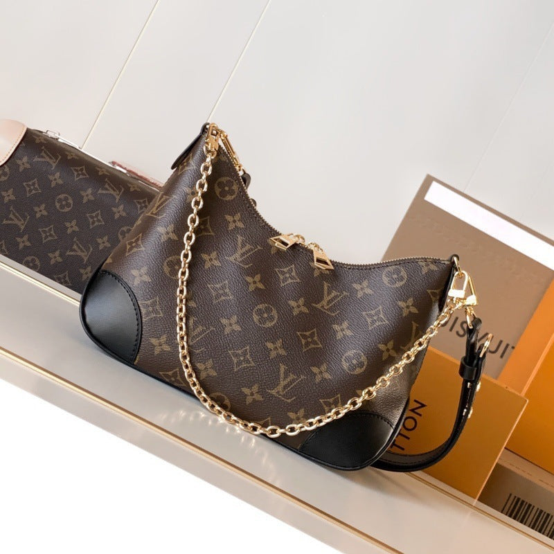 A Louis Vuitton monogram shoulder bag in brown coated canvas with black leather trim and a gold-tone chain strap, displayed on a shelf with branded packaging boxes.