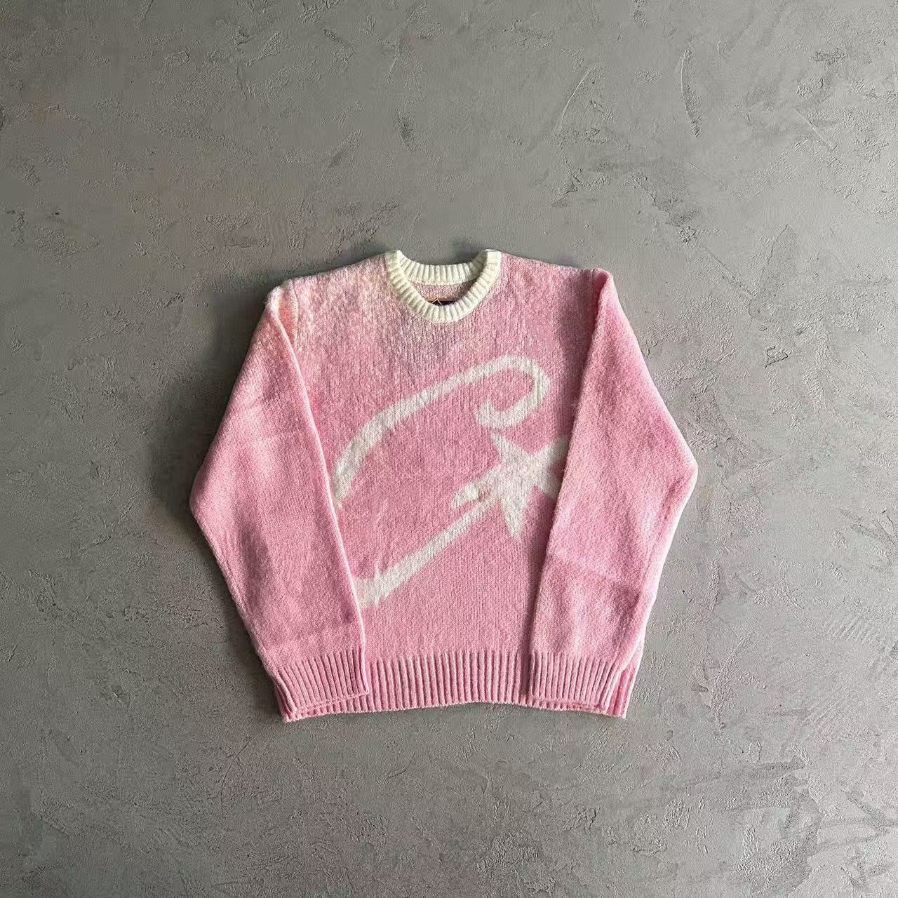 Pink sweater with a white logo on a gray surface