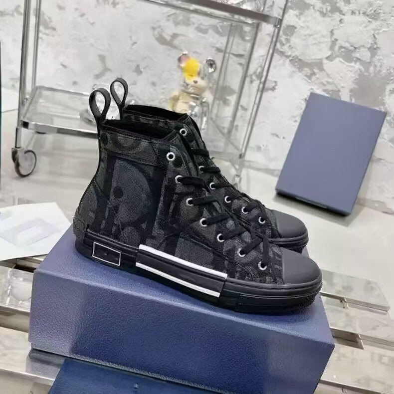 A pair of black high-top sneakers with a subtle monogram pattern, displayed on a blue shoebox against a marble background.