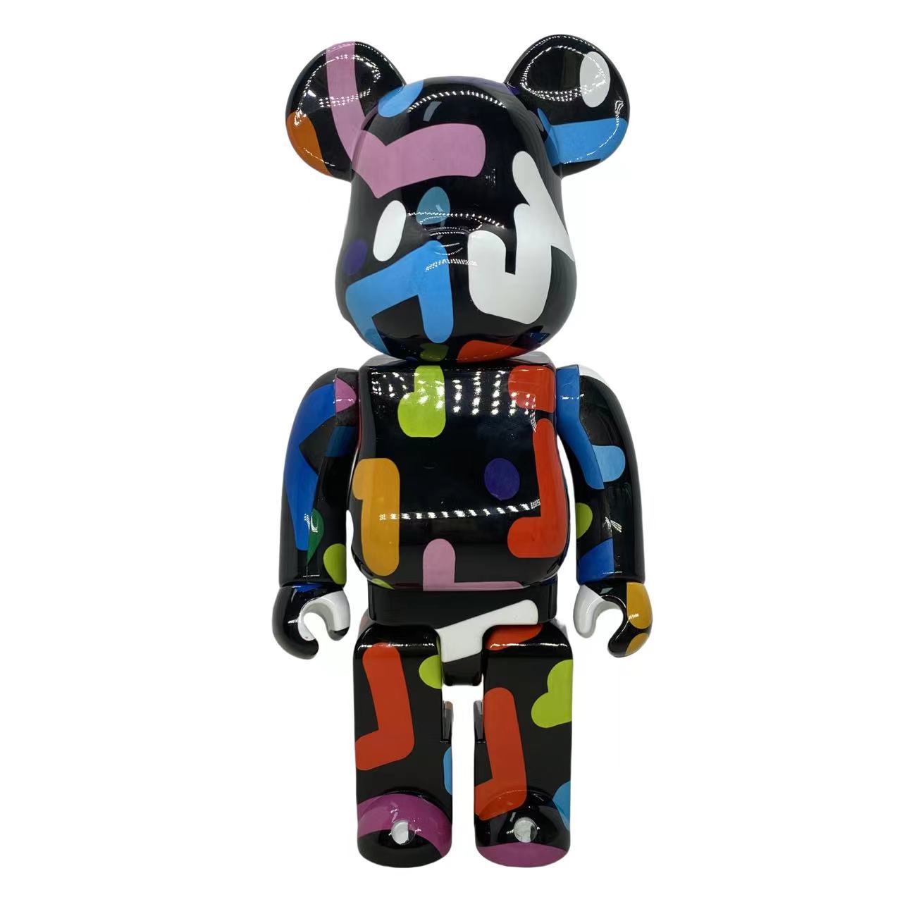 A collectible bear figure with a glossy black base covered in colorful abstract paint splatters and shapes, photographed against a solid white background.