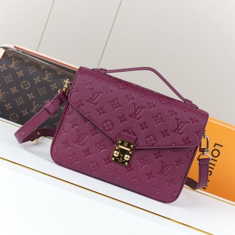 A purple Louis Vuitton monogram embossed leather shoulder bag with gold-tone hardware, displayed on a white surface with a Louis Vuitton monogram pouch and orange box in the background.