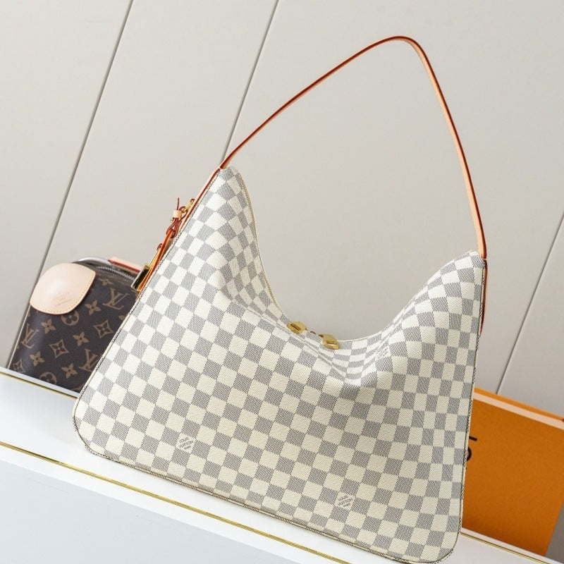 A Louis Vuitton shoulder bag in Damier Azur canvas with a gray and off-white checkerboard pattern, featuring a thin brown leather shoulder strap and gold-tone hardware, displayed on a white shelf next to a Louis Vuitton monogram pouch.