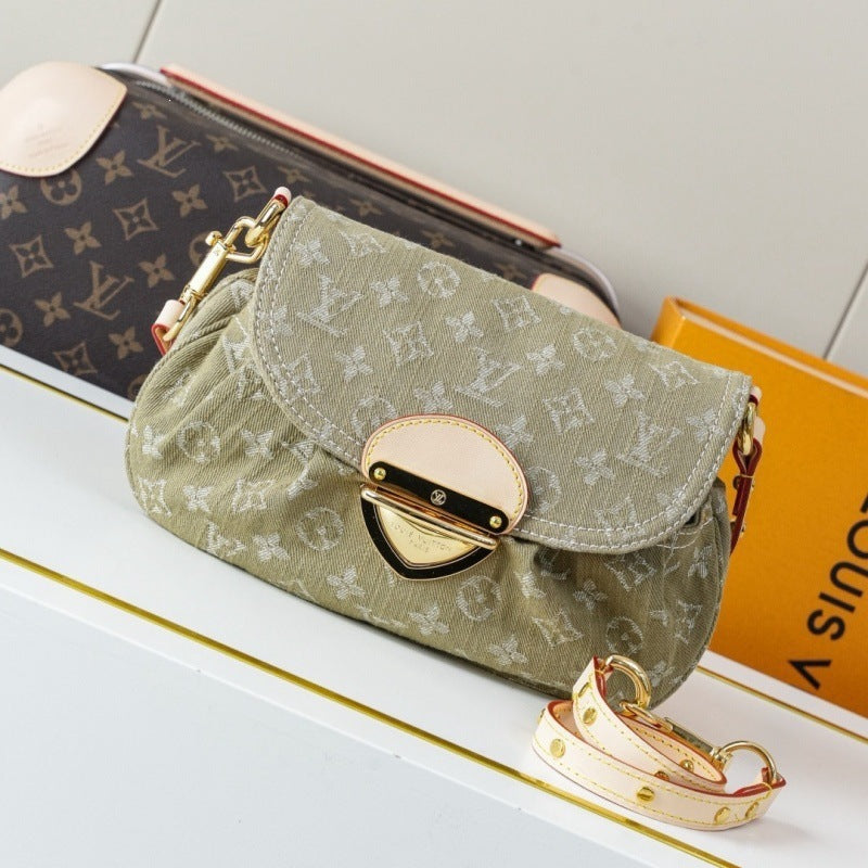 A Louis Vuitton monogram canvas shoulder bag in olive green, displayed on a white shelf next to a brown monogram pouch and an orange Louis Vuitton box. The bag features a cream leather turn-lock clasp and a matching cream detachable shoulder strap.