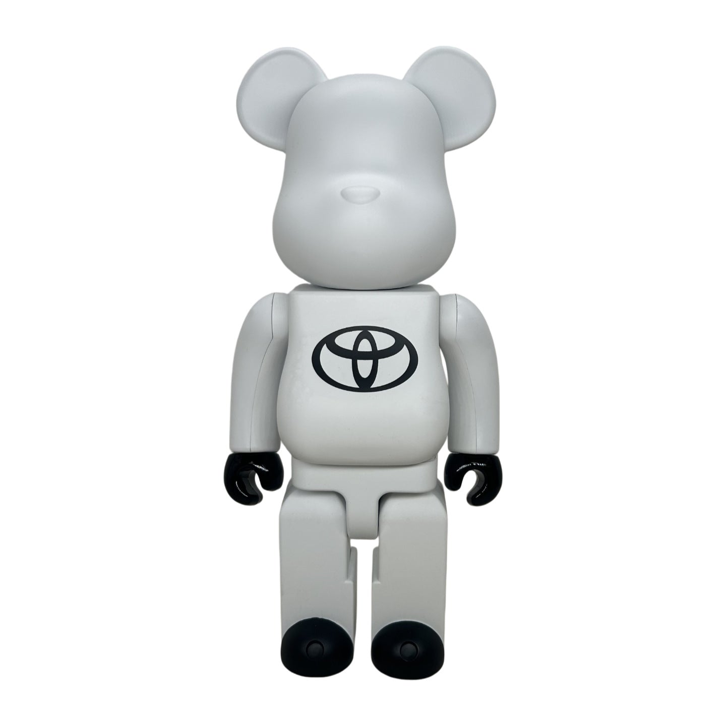A white bear-shaped collectible figure with black hands and feet, featuring a black Toyota emblem on the chest, set against a plain white background.