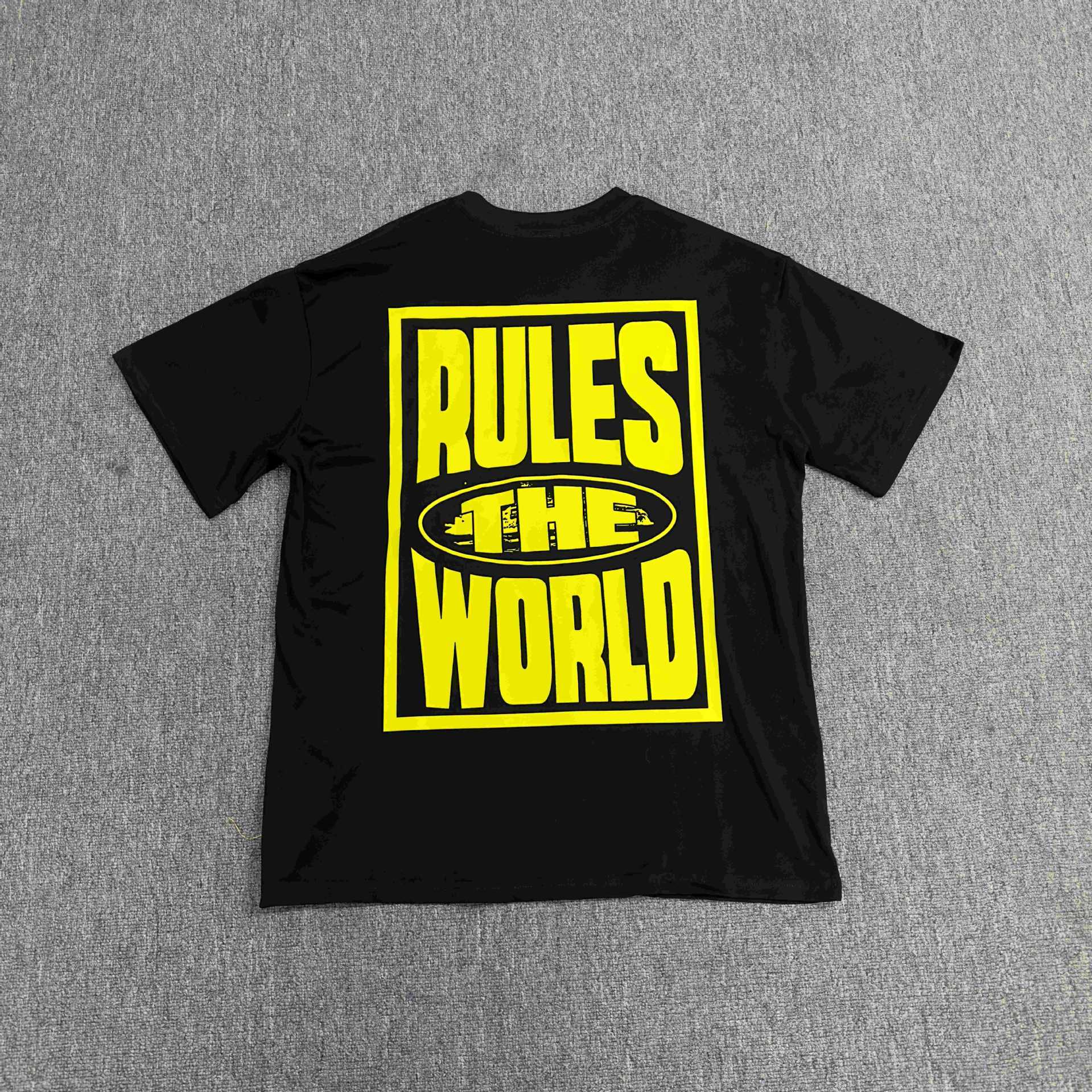 Black t-shirt with yellow text 'RULES THE WORLD' on a gray background