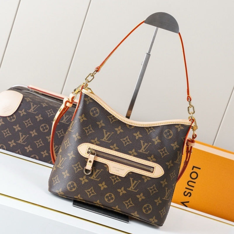 Louis Vuitton monogram shoulder bag in brown coated canvas with beige leather trim and gold-tone hardware, displayed on a stand with part of a matching zip pouch and an orange Louis Vuitton box in the background.