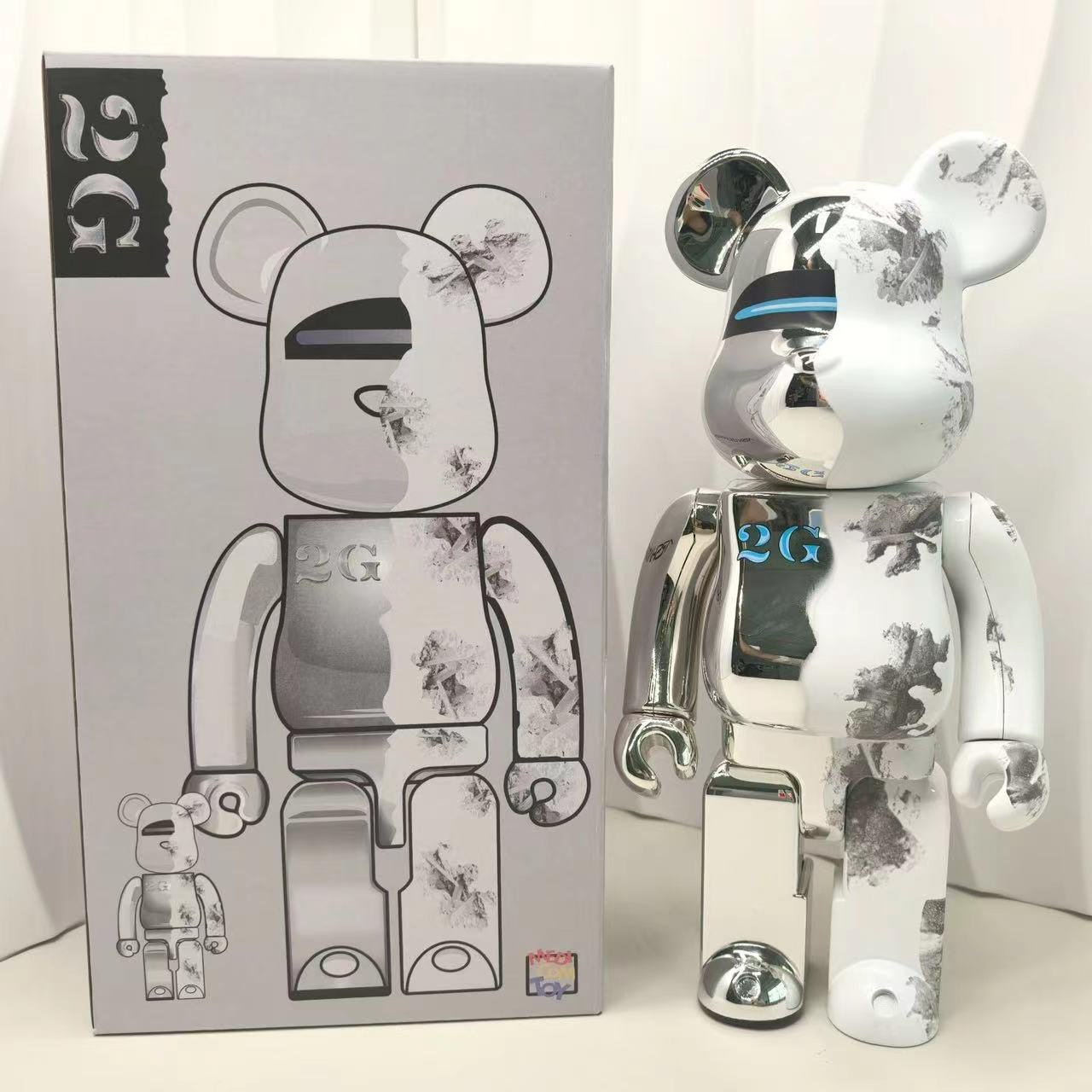 A shiny silver and white bear-shaped collectible figure with black floral-style splatter markings stands beside its matching product box. The box shows a large version of the bear face and a small version at the bottom, with stylized '26' graphics on the packaging.