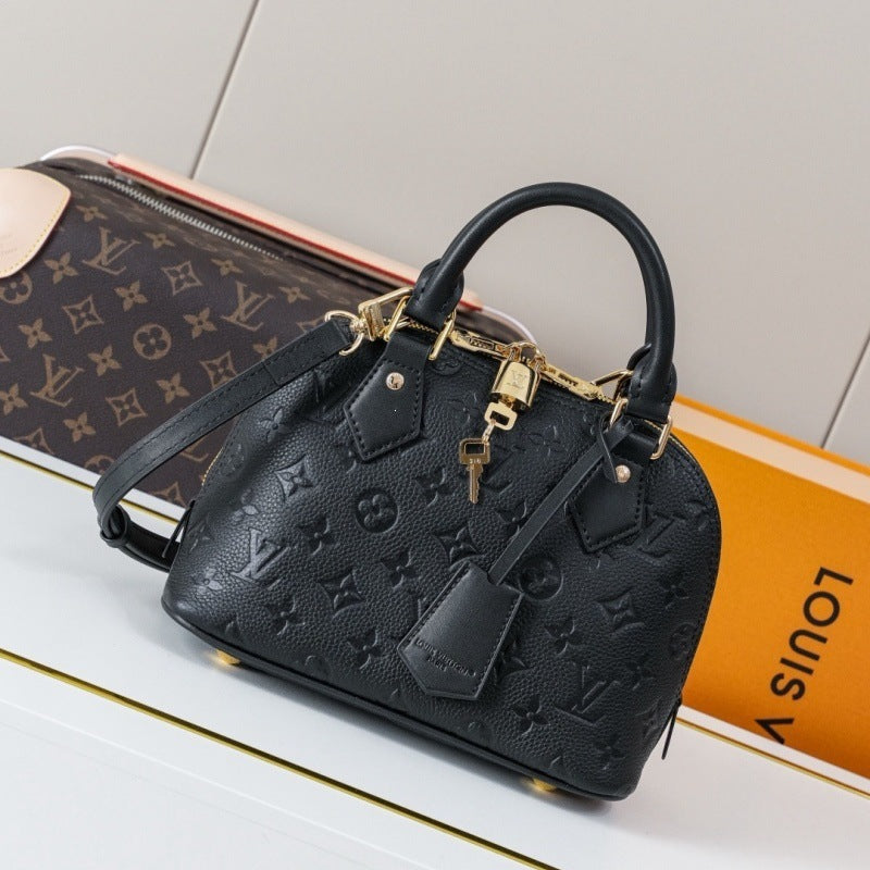 A black Louis Vuitton monogram embossed leather handbag with gold-tone hardware, displayed on top of a brown monogram pouch and an orange Louis Vuitton box.
