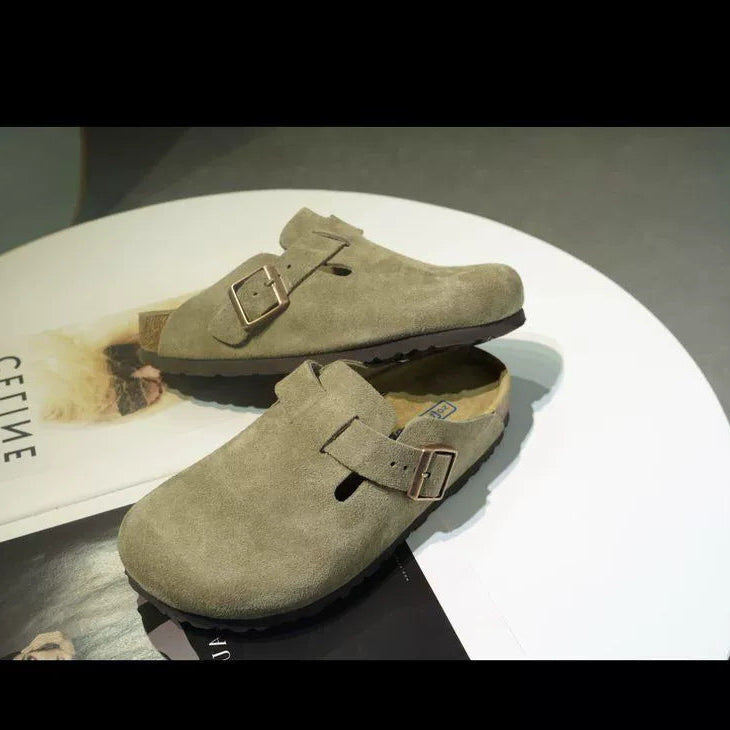 Pair of green suede shoes with buckles on a white surface.