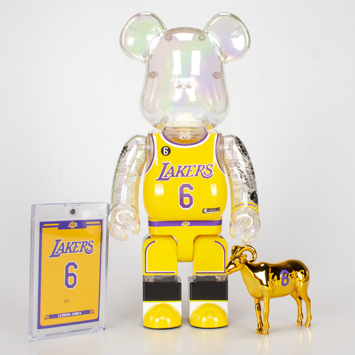 A translucent iridescent bear figure wearing a yellow Los Angeles Lakers jersey with the number 6, shown with a matching Lakers card and a small metallic gold goat figure on a white background.