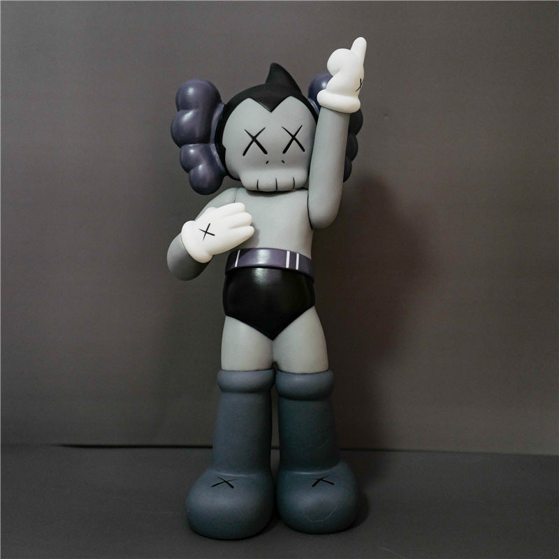 A stylized toy figure resembling a cartoon character, standing against a plain gray studio background. The figure has a pale gray face and torso, black shorts, dark blue-gray boots, and dark purple hair, with white raised hands and X-shaped eyes.