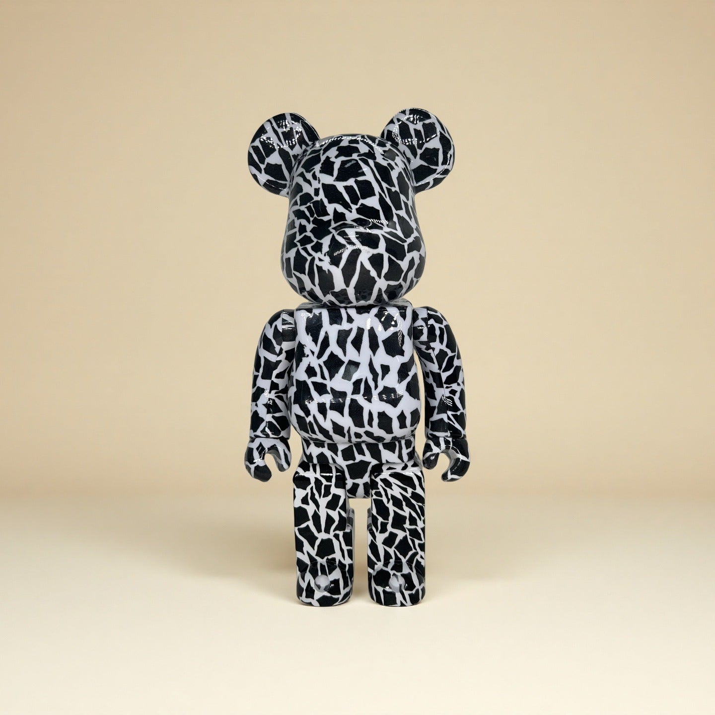 A collectible bear-shaped plush toy with a black and white organic splatter pattern, standing upright against a solid beige background.