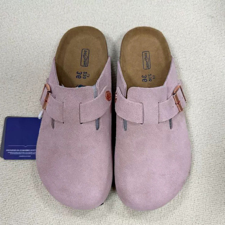 Pair of pink suede clogs with a tag on a light gray background