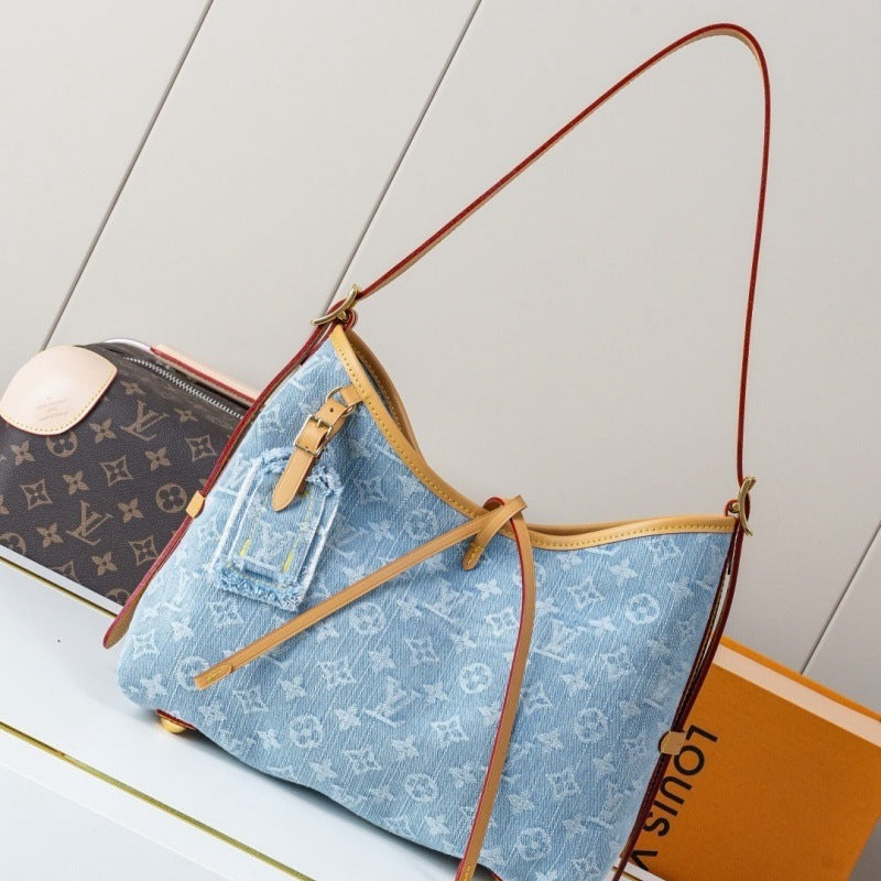 A light blue Louis Vuitton canvas shoulder bag with a monogram pattern, tan leather trim, and a brown leather strap, styled next to a brown Louis Vuitton monogram pouch and an orange Louis Vuitton box.