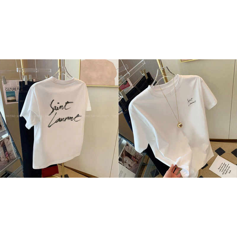 Two views of a white short-sleeve T-shirt on hangers in a boutique setting. The left view shows large black script text reading 'Saint Laurent' across the chest, while the right view shows a smaller matching script logo on the left chest.