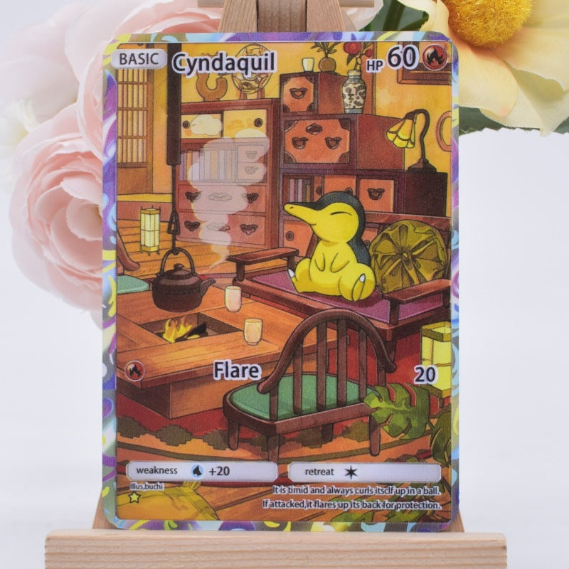 A Cyndaquil Pokémon trading card displayed upright on a small wooden stand, with pink and yellow flowers blurred in the background.