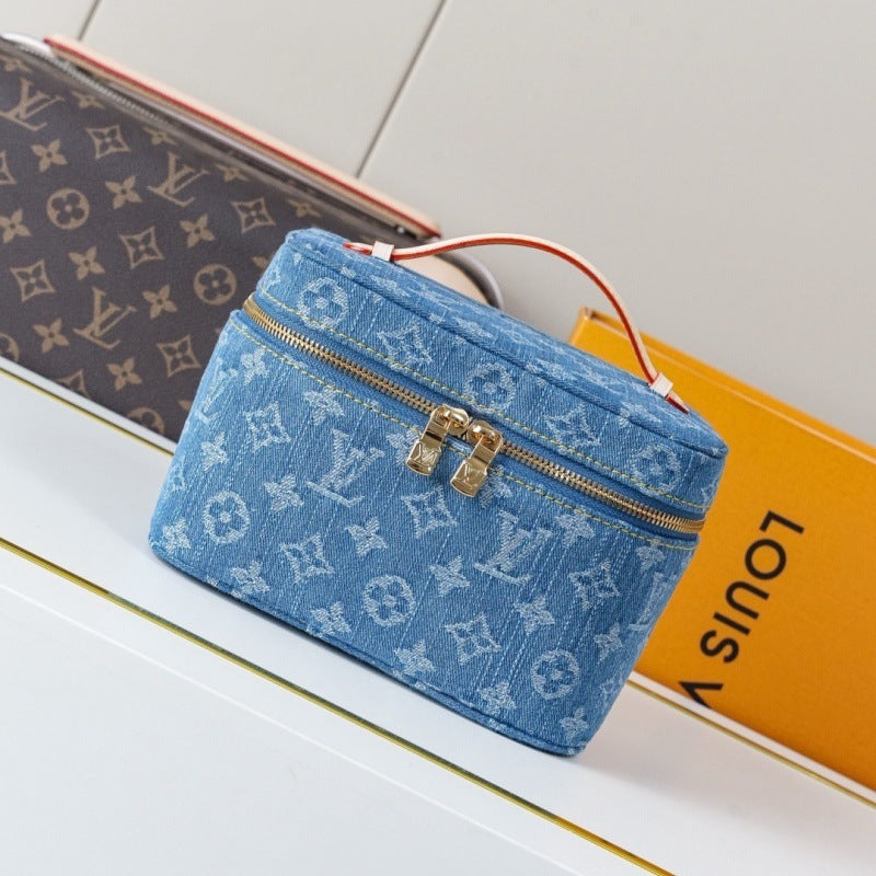 A blue monogram canvas cosmetic bag with a top handle and gold-tone hardware, styled on a white surface next to a Louis Vuitton box and a brown monogram clutch.