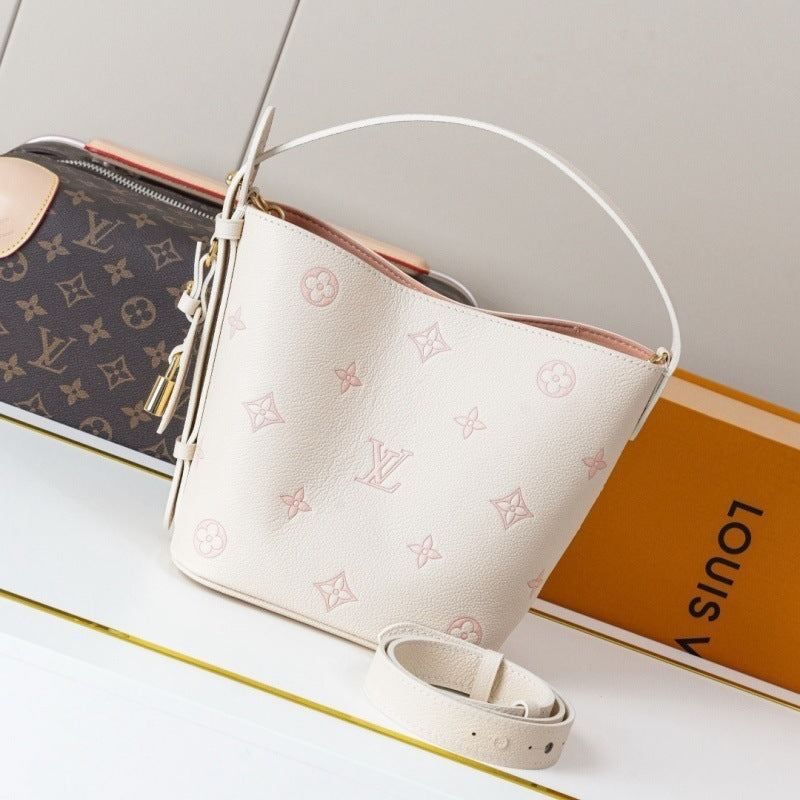 White handbag with monogram pattern on a white surface with a Louis Vuitton book in the background.