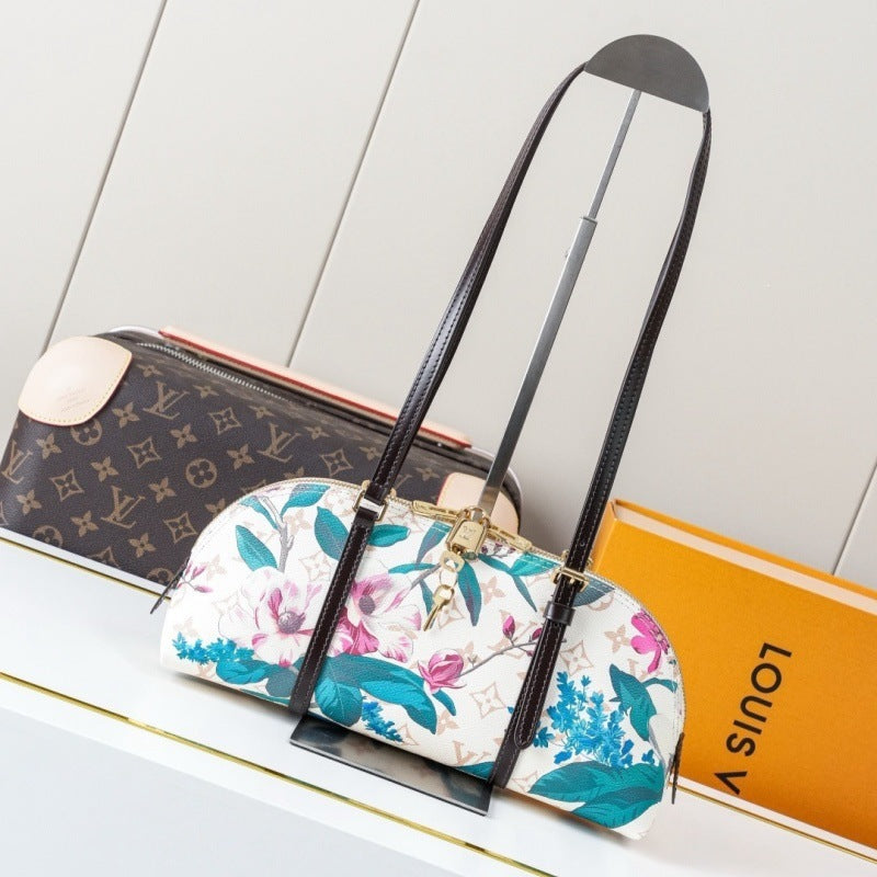 A Louis Vuitton floral dome shoulder bag with a long black strap, displayed on a stand next to its brown monogram packaging and an orange Louis Vuitton box on a white shelf.