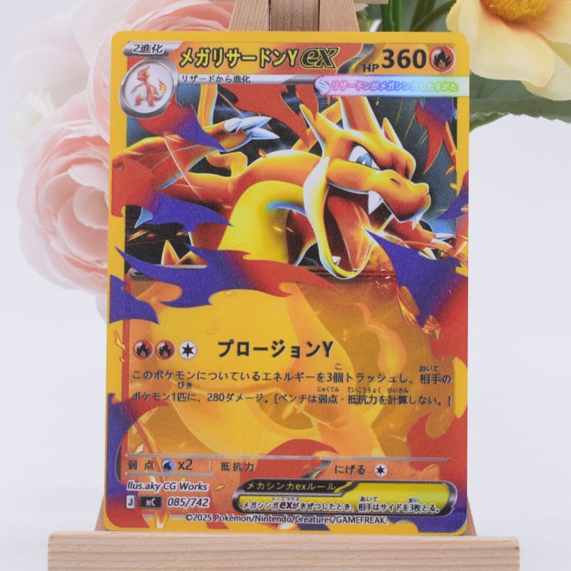 A Japanese Pokémon Charizard Y EX trading card displayed upright on a small wooden stand, with pink and yellow flowers blurred in the background.