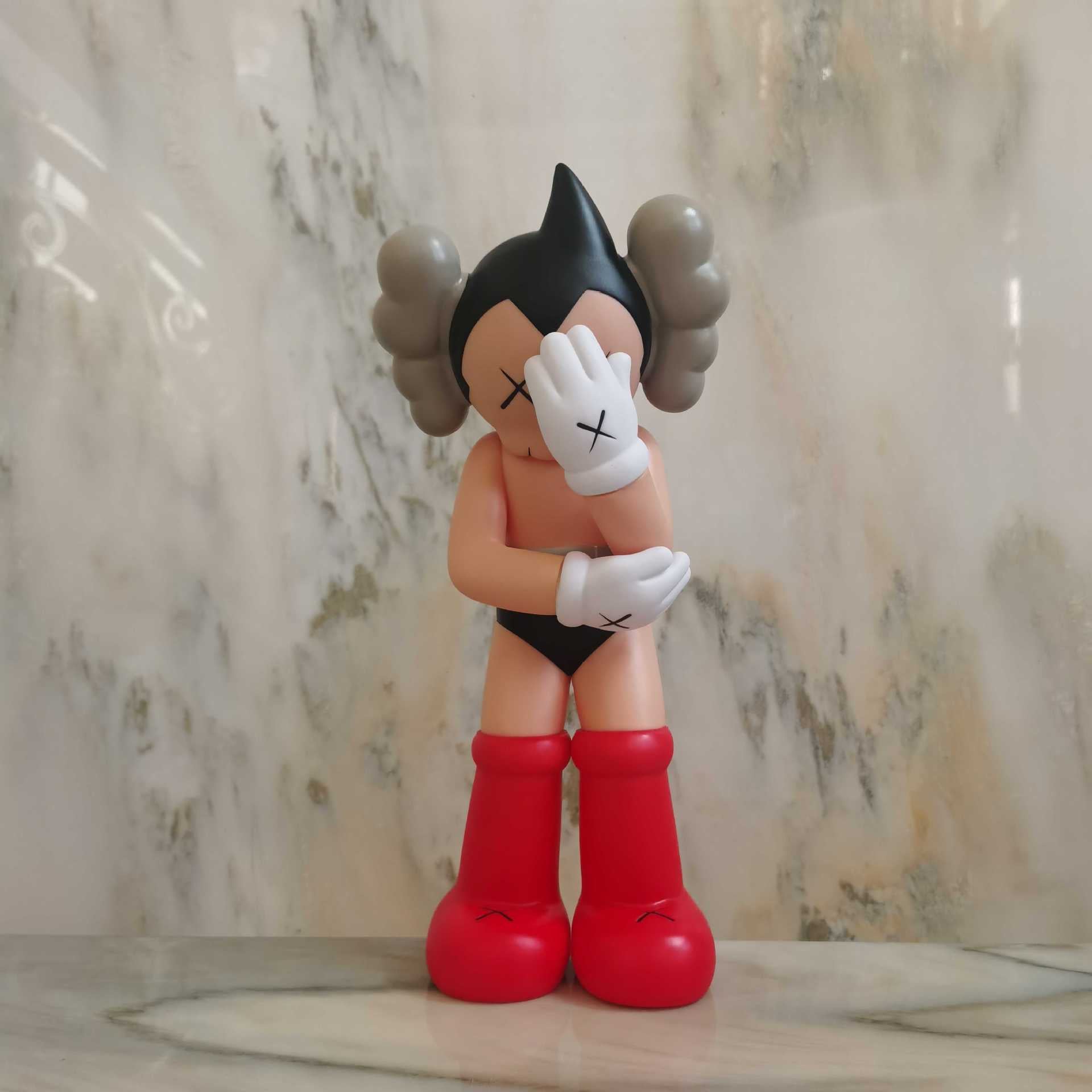 A stylized toy figurine of a character with black hair in twin buns, white gloves with black X marks, red boots, and black underwear, standing on a marble-like surface against a marble-patterned wall.