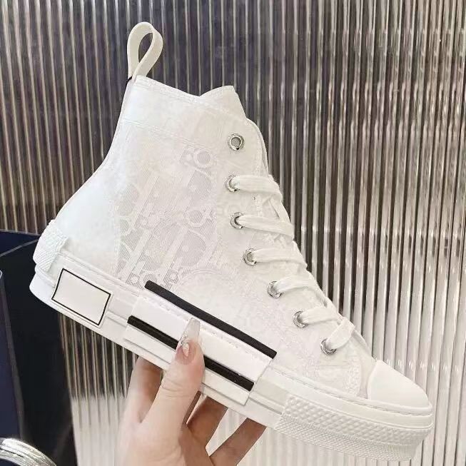 A high-top white sneaker with an embossed monogram pattern, held by a hand against a metallic ribbed background.
