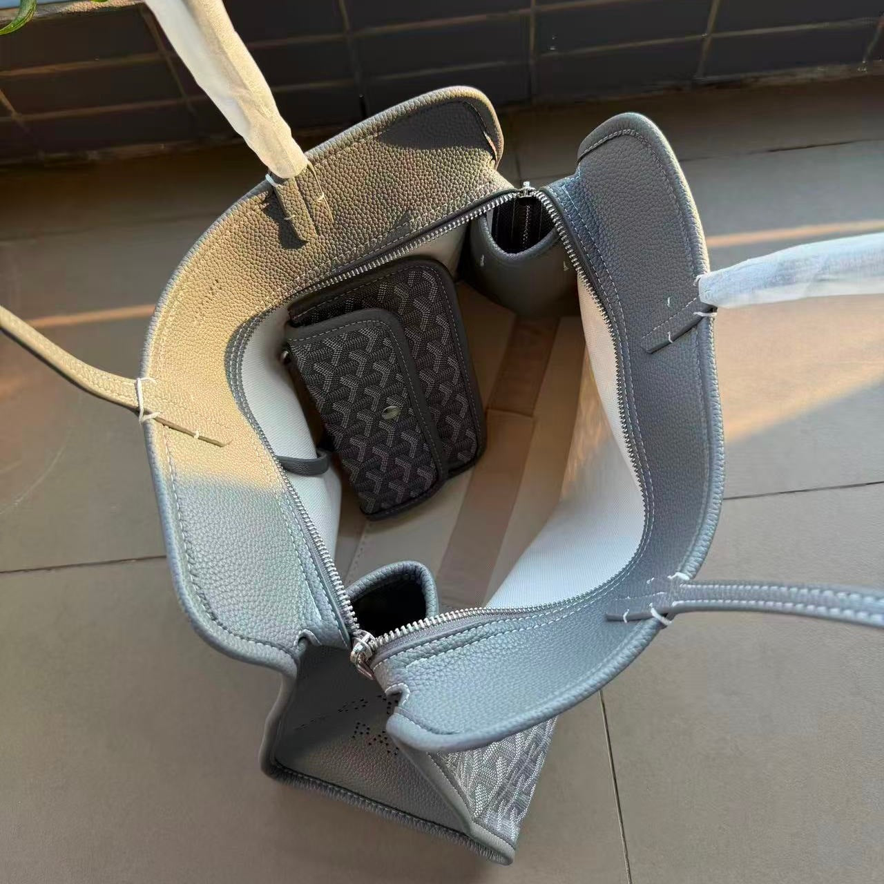 Open handbag with phone inside on a tiled floor