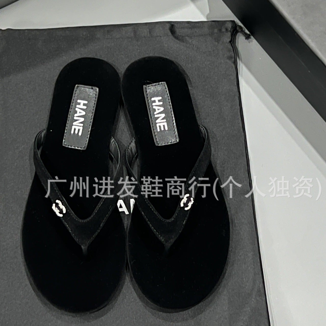 Black sandals with 'HANE' branding on a gray drawstring bag.