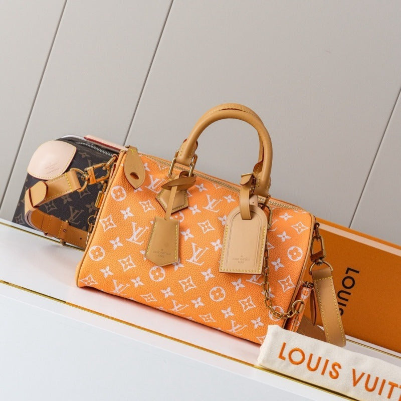 An orange Louis Vuitton Speedy handbag with the classic monogram pattern, displayed on a white shelf next to a Louis Vuitton box and another bag.