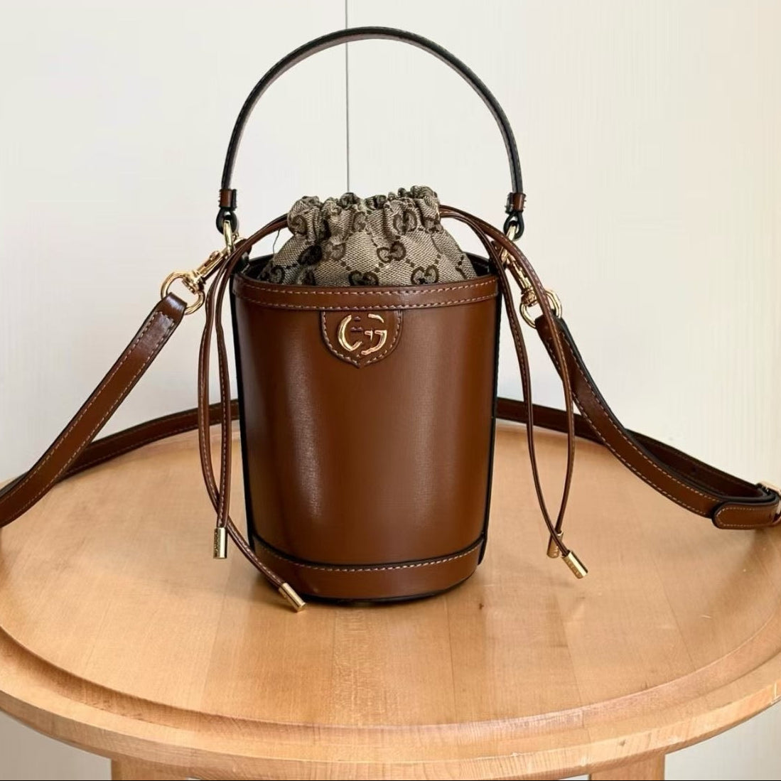 A brown leather bucket bag with a drawstring top, gold-tone hardware, and a Gucci monogram pattern lining, displayed on a round wooden table. Chinese text in the top-left corner shows the style number 760201 and dimensions 11.
