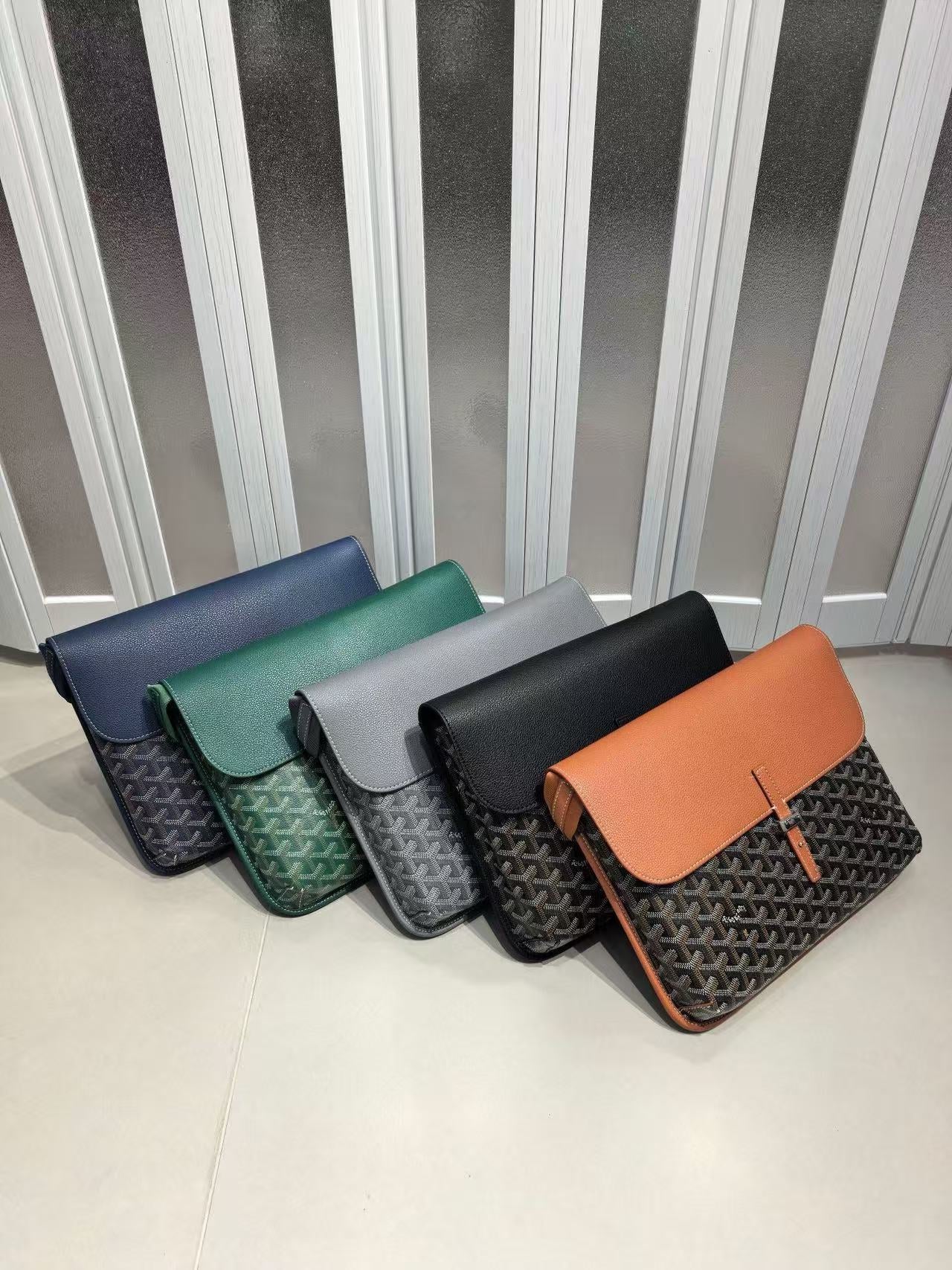 Five different colored handbags arranged in a row on a light surface with a striped background.