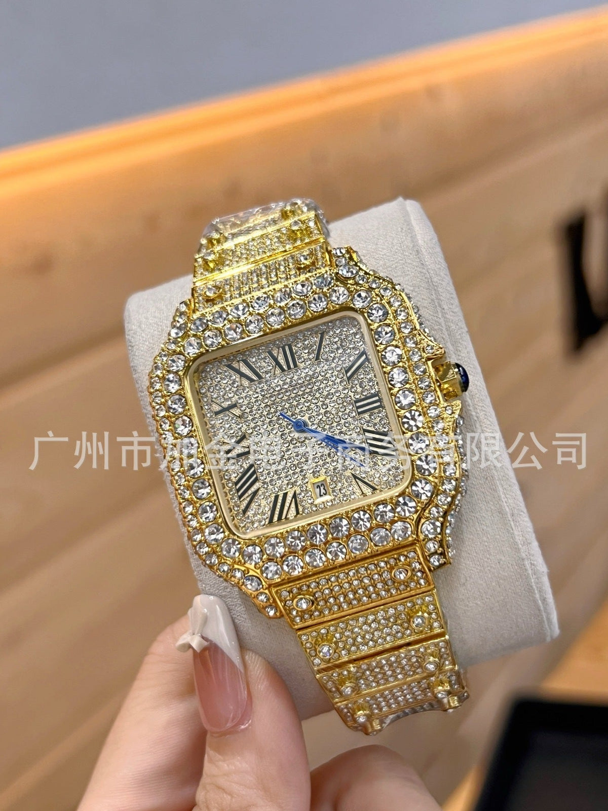 A gold-tone watch with a diamond-encrusted face and matching diamond-covered bracelet, held in a hand against a warm wood background.