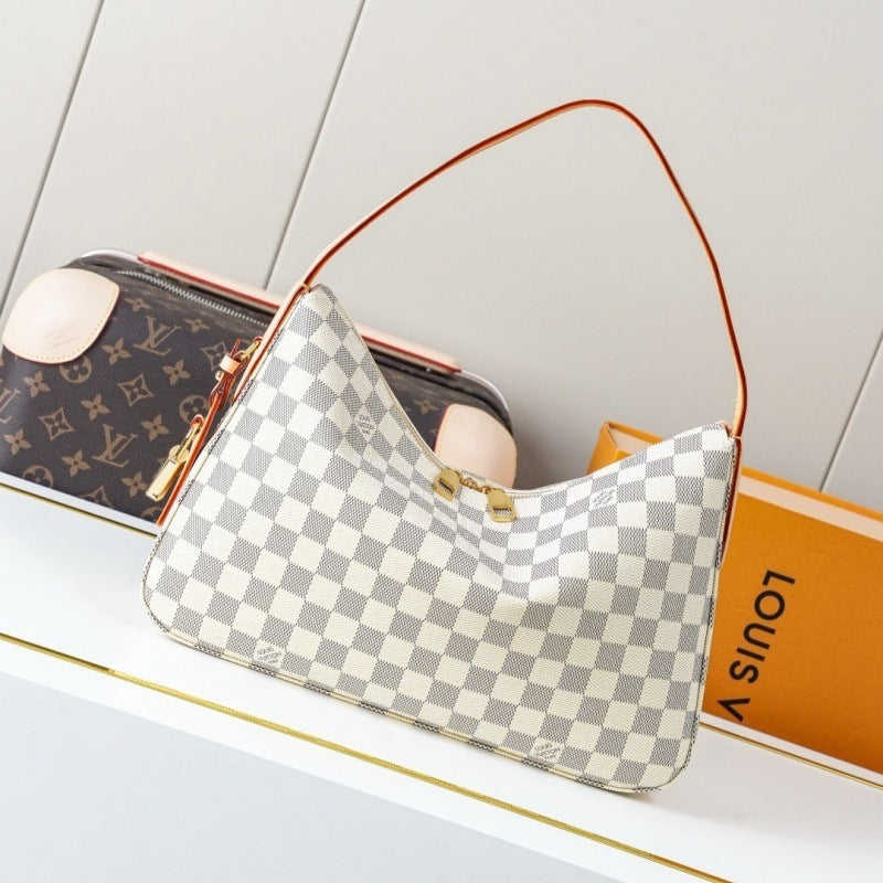 A Louis Vuitton shoulder bag in Damier Azur canvas with a gray and white checkerboard pattern, brown leather strap, and gold-tone hardware, displayed on a white shelf next to a Louis Vuitton monogram pouch and orange box.