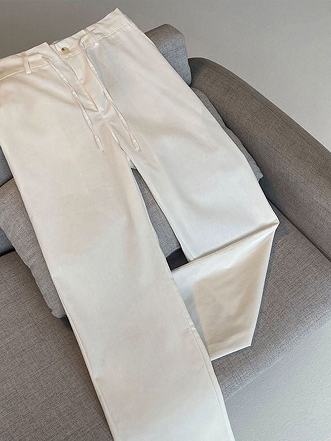 A pair of off-white or cream-colored wide-leg pants laid flat on a gray fabric armchair. The pants have a relaxed straight-leg fit, a front fly, and a small gold-toned button closure at the waistband.