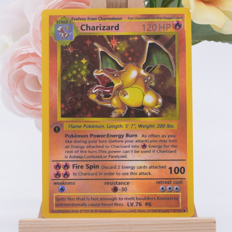 A Charizard Pokémon trading card displayed upright on a small wooden stand, with soft pink flowers blurred in the background.